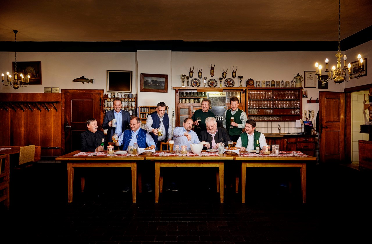 Viele Männer sitzen in einer Gaststube am Tisch und trinken Bier.