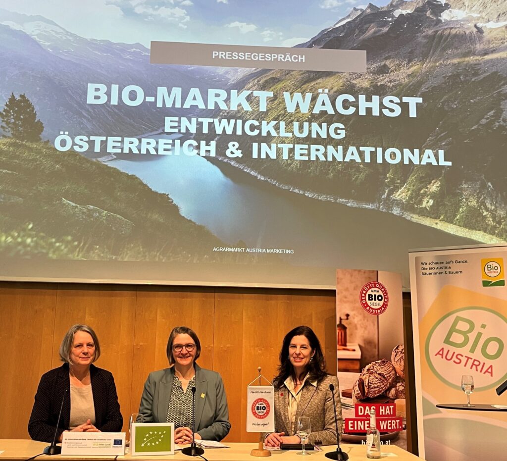 Drei Frauen sitzen bei einer Pressekonferenz vor einer Projektion.