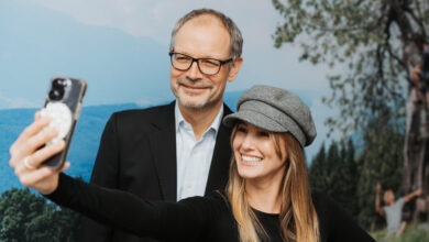 Ein älterer Mann und eine junge Frau machen zusammen ein Selfie und lachen.