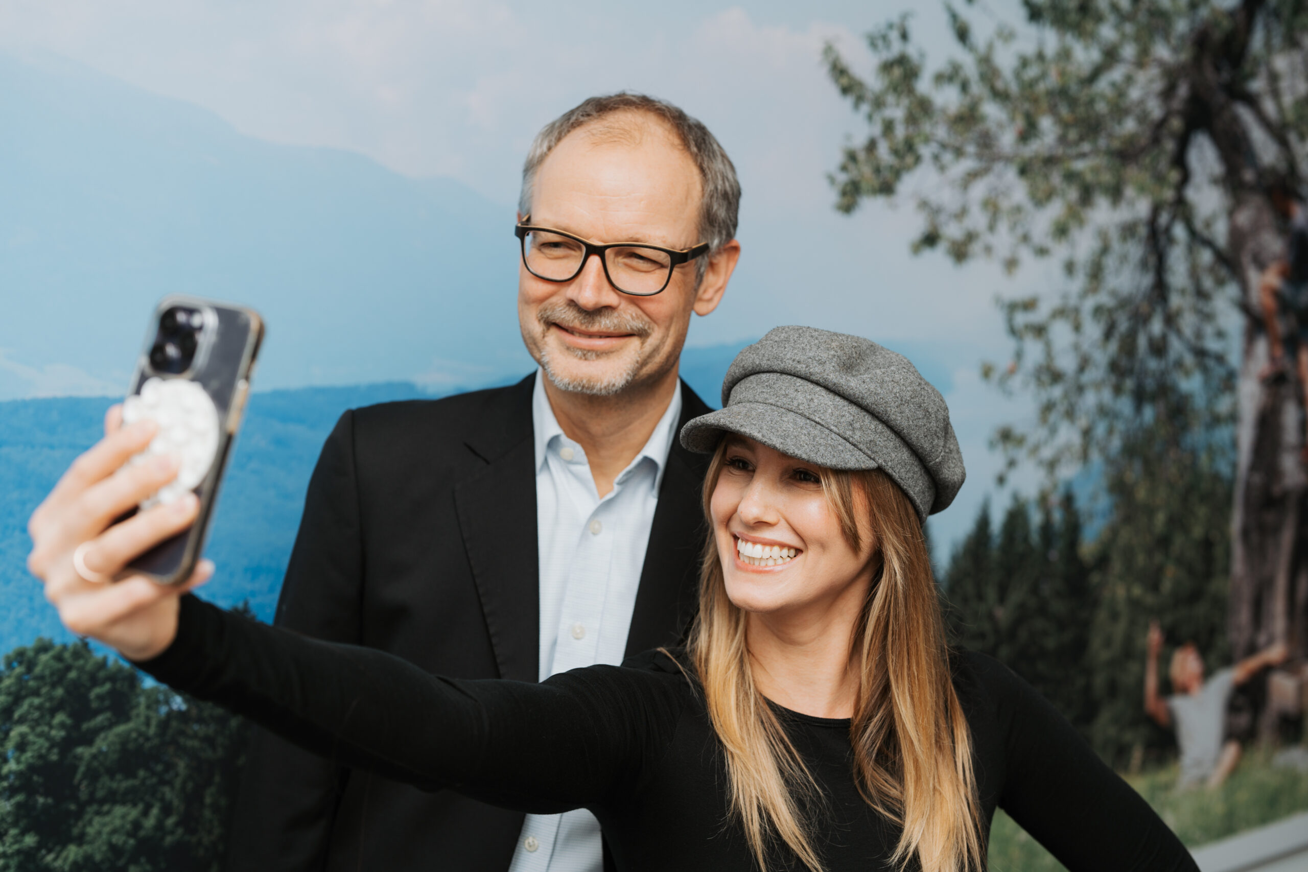 Ein älterer Mann und eine junge Frau machen zusammen ein Selfie und lachen.