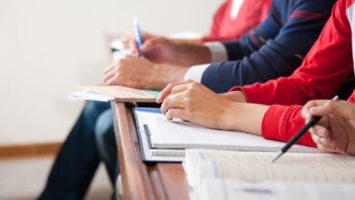 Nahaufnahme von Händen: Studierende in einem Klassenzimmer.