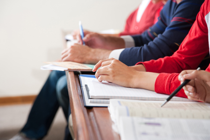 Nahaufnahme von Händen: Studierende in einem Klassenzimmer.