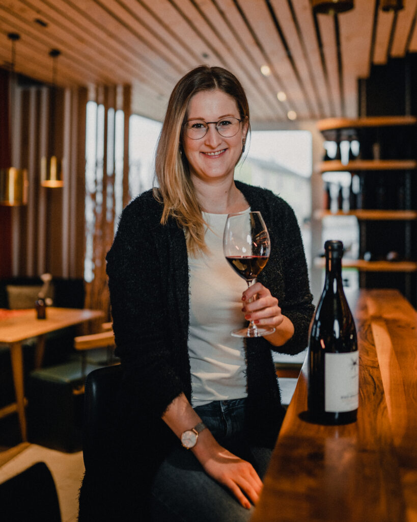 Eine Frau sitzt an einer Bar und trinkt ein Glas Rotwein.