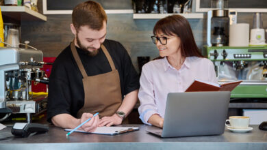 Symbolfoto zweier Personen hinter dem Tresen mit Laptop und Schreibmaterial © Valeriy_G iStock Getty Images Plus