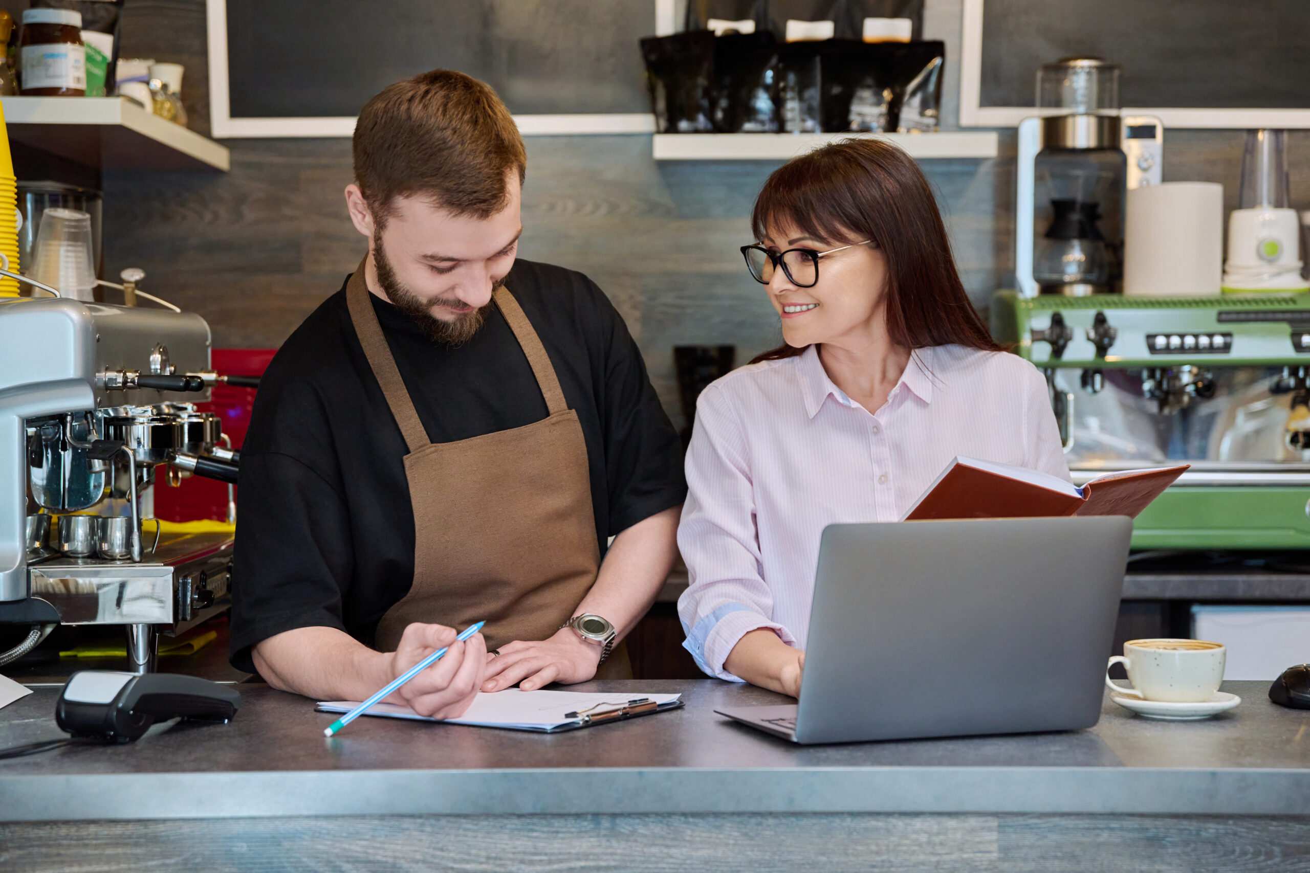 Symbolfoto zweier Personen hinter dem Tresen mit Laptop und Schreibmaterial © Valeriy_G iStock Getty Images Plus