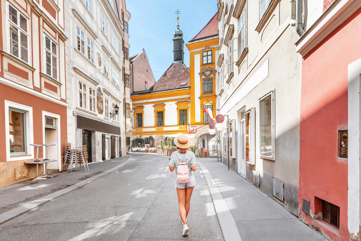 Junge asiatische Frau mit Rucksack und Hut zu Fuß auf der Stadtstraße in Europa.