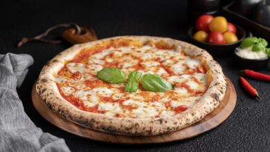 Pizza mit frischem Basilikum, Tomaten und Käse auf Holzplatte.